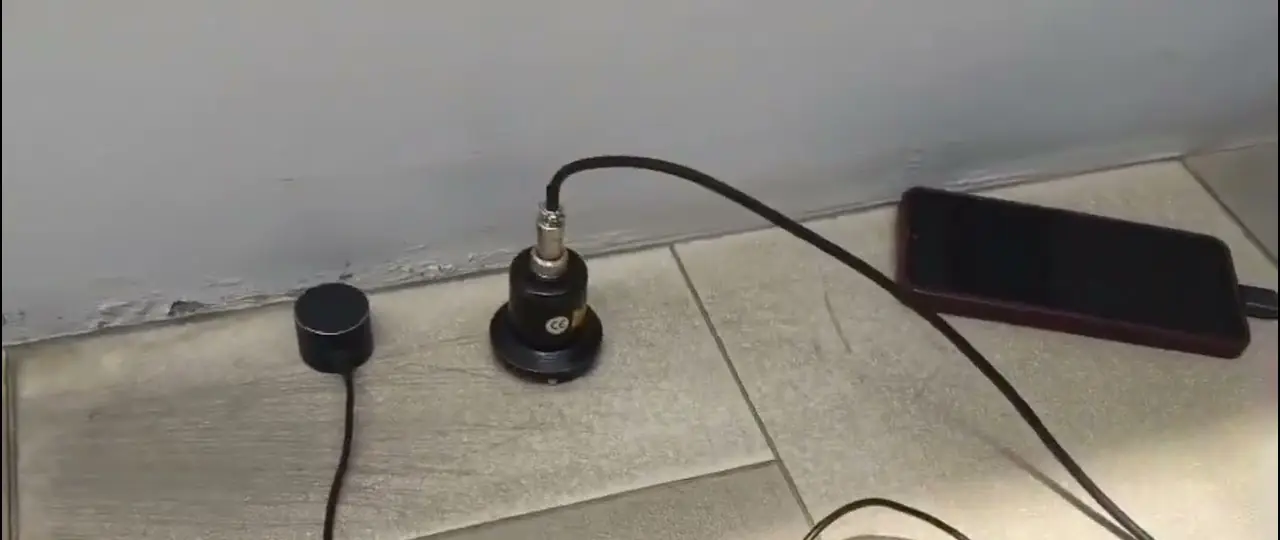 Sensor detektor akustik di atas lantai keramik, tersambung ke penguat suara, saat mencari titik pipa bocor
